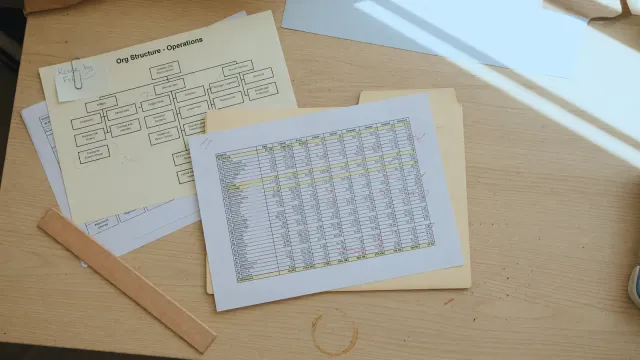 Printed Gartner survey table on a desk next to an org-chart printout and an unpaid cloud invoice, office fluorescent light, no logos