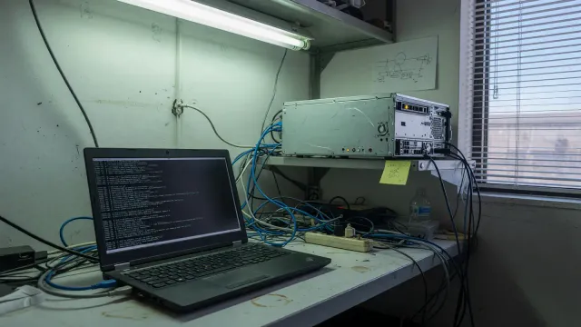 Developer laptop next to a small server rack in an office, terminal on screen with no readable text, cool overhead light, no logos
