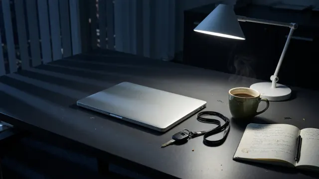 Laptop terminal showing a home directory listing with .claude.json next to a hardware key on a desk, cool lamp light, no logos