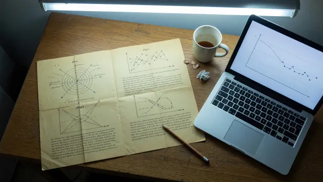Desk with a printed 1911 physics paper beside a laptop showing a sparse loss curve, cool overhead light, no logos
