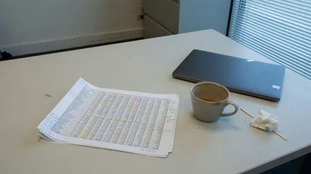 A conference table with a printed budget spreadsheet, a laptop, and a coffee cup, cool office daylight, no logos or readable UI
