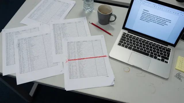 Printed experiment log on a desk with one line highlighted red, a laptop showing a short summary beside it, cool office light, no logos