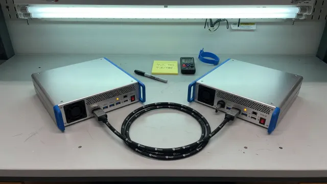 Two desktop workstations linked by a short Thunderbolt cable on a lab bench, cool overhead light, no logos